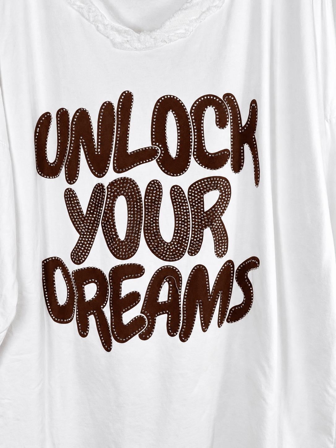 Photo retouchée du message brun Unlock Your Dreams et de ses strass sur la tunique blanche.