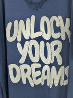 Gros plan des lettres claires et des strass sur la tunique bleu marine Unlock Your Dreams.