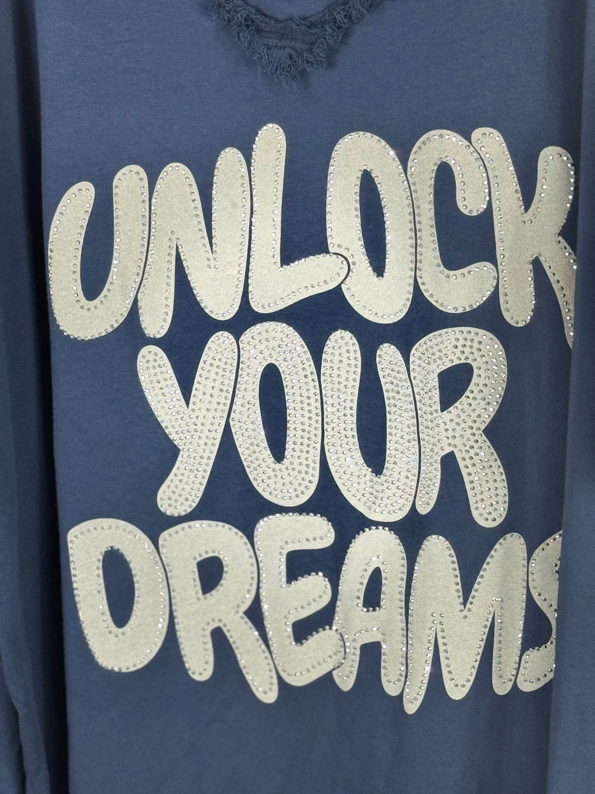 Gros plan des lettres claires et des strass sur la tunique bleu marine Unlock Your Dreams.