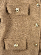 Détail de la texture bouclée camel, des boutons dorés et des rabats décoratifs de la veste Giulia