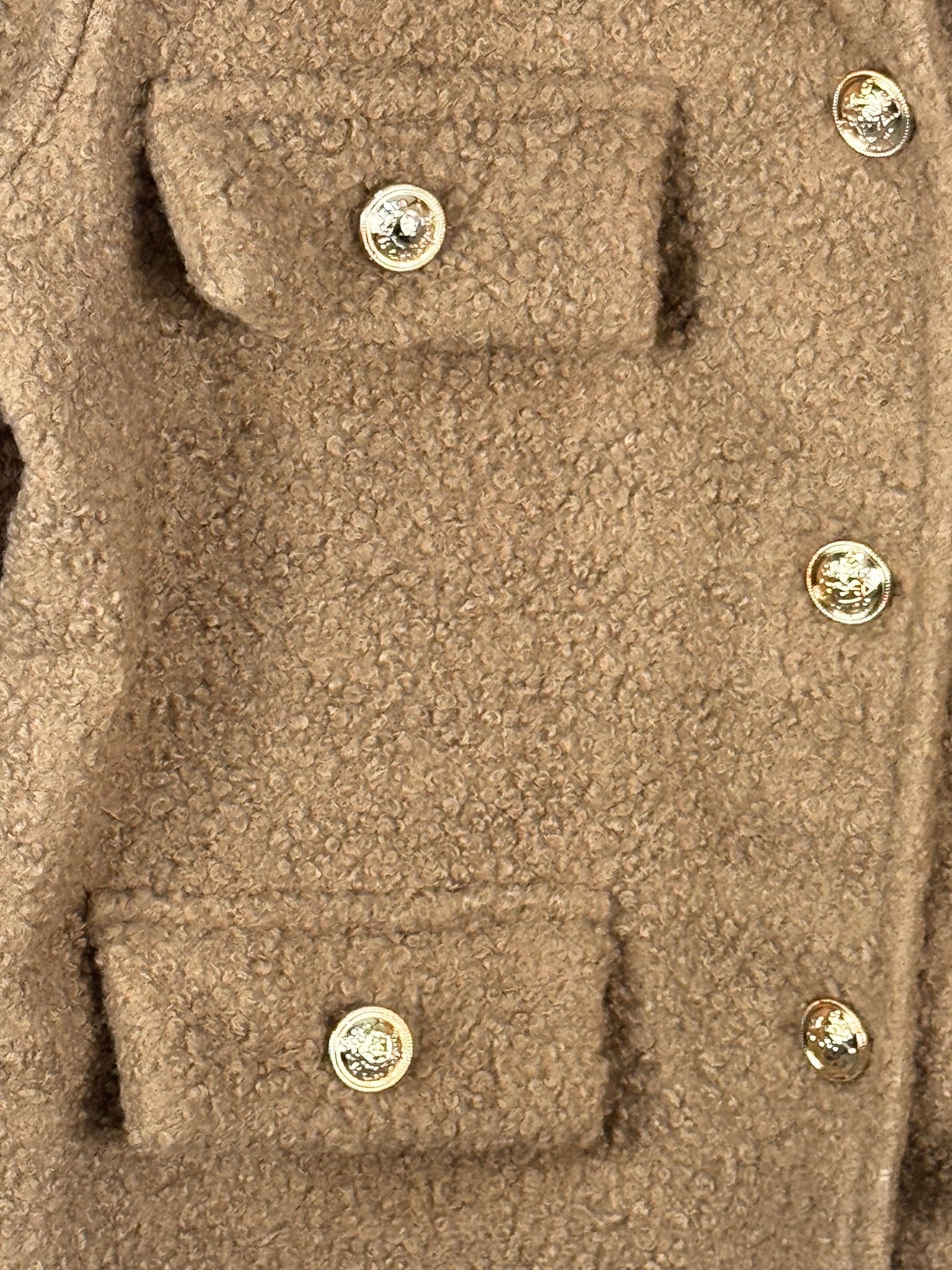 Détail de la texture bouclée camel, des boutons dorés et des rabats décoratifs de la veste Giulia