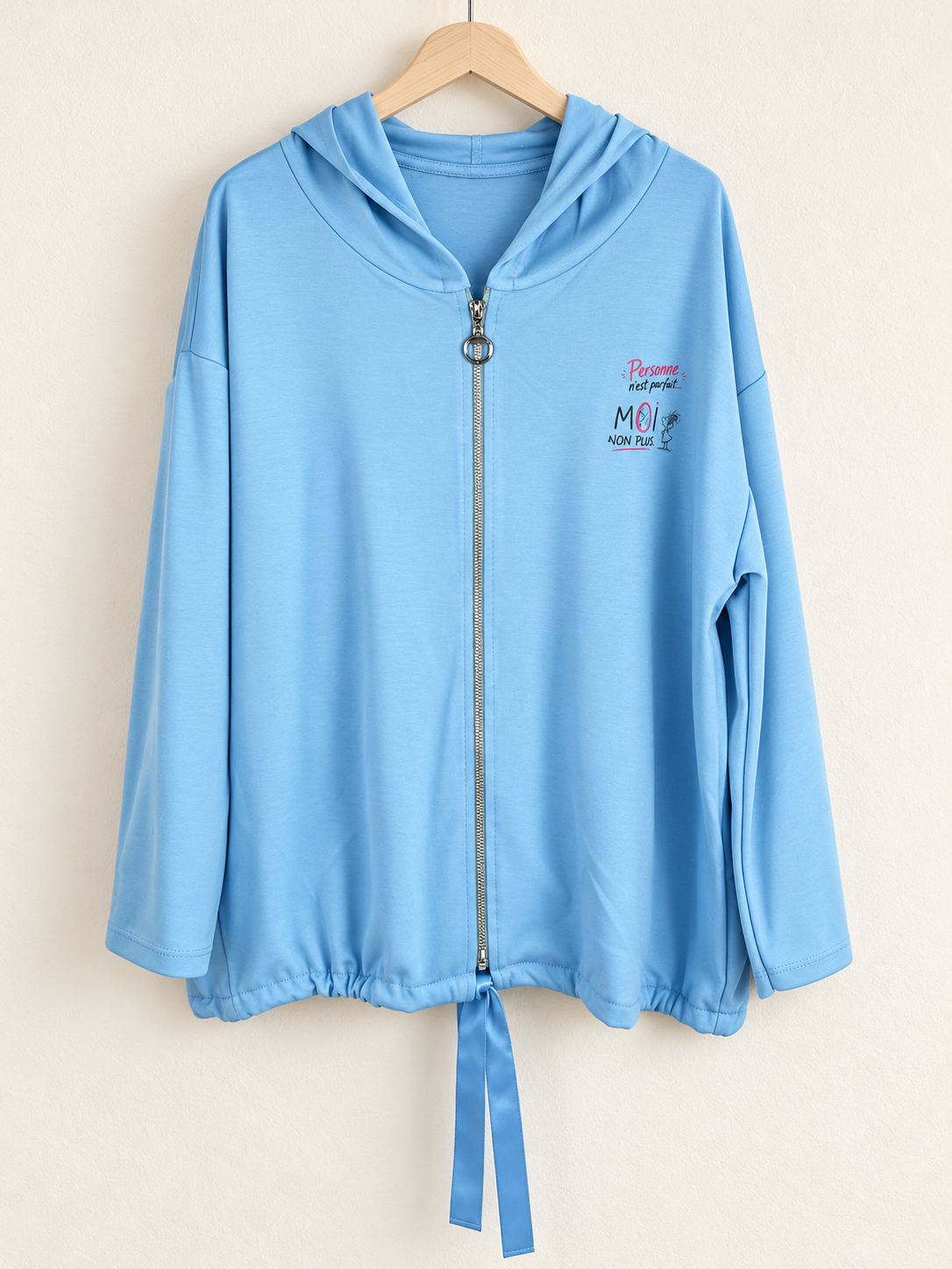 Veste bleu ciel sur cintre, photo retouchée montrant le petit message côté cœur, le zip à anneau et les rubans satinés